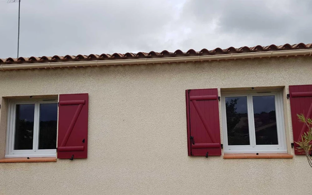 Façade provençale avec deux fenêtres et des volets battants rouges