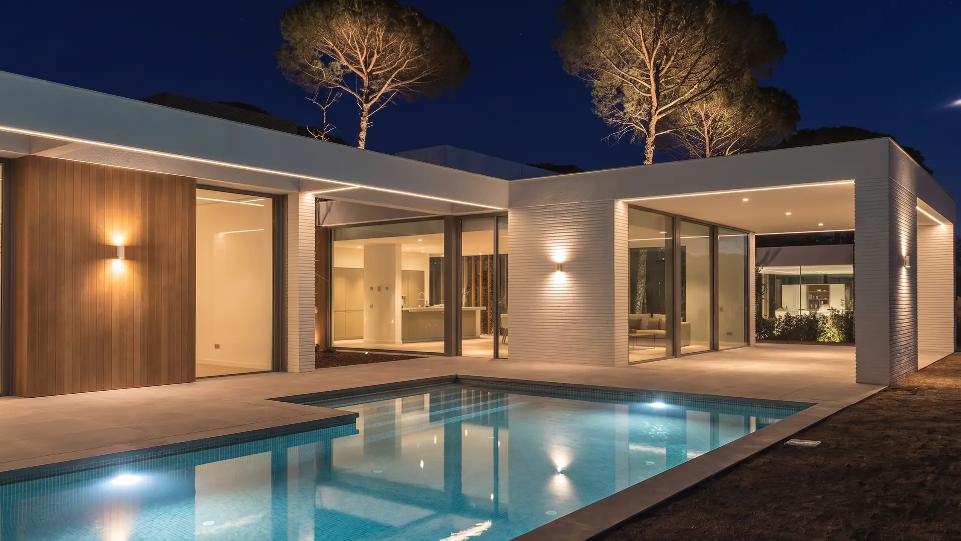 Villa éclairée au bord d'une piscine, grandes baies vitrées